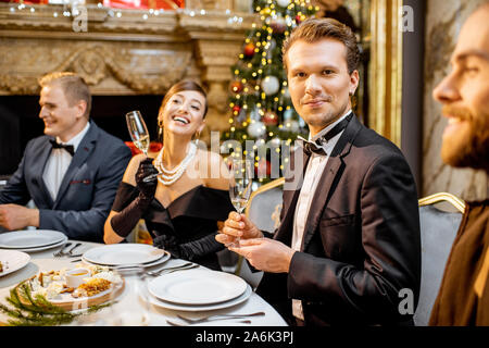 Ritratto di un bel ben vestito uomo seduto durante una cena di gala con gli amici per la Vigilia di Capodanno presso il ristorante di lusso o home Foto Stock