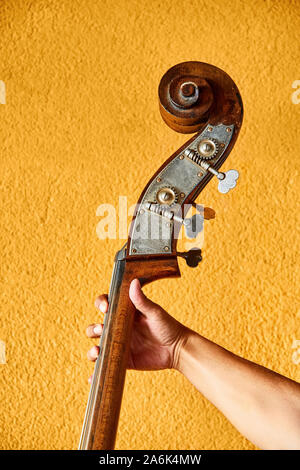 Stretta di mano di un maschio di musicista jazz detiene il contrabbasso contro la parete gialla sullo sfondo Foto Stock