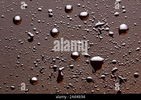 Lucido di gocce di acqua su un colore marrone scuro moody superficie. Abstract sfondo con close up vista aerea. Foto Stock