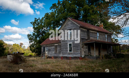 Casa abbandonata circondata da alberi in autunno con cumulus nubi nel cielo blu Foto Stock