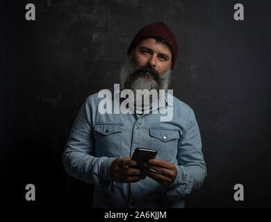 Ritratto di uomo con la barba e baffi. Jeans camicia, cappello di lana e mobili in mano. Concetto Movember Foto Stock