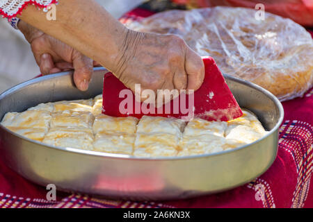Vecchia donna rendendo tradizionale bulgaro con torta di formaggio bianco chiamato banitsa. Il taglio dei pezzi con il vecchio strumento. Foto Stock