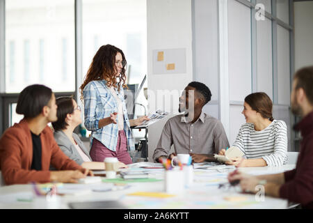 Ritratto di creative team business sorridendo allegramente mentre il progetto di pianificazione durante la riunione in ufficio, concentrarsi sul giovane donna presentare idee in piedi Foto Stock