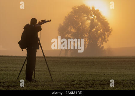 Silhouette di puntamento cacciatore con un fucile nel campo su una bella foschia mattutina Foto Stock