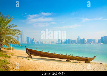 Arabo moderno città di Abu Dhabi. Paesaggio e paesaggio panorama con la barca di legno in primo piano sulla spiaggia. Emirati Arabi Uniti. Foto Stock