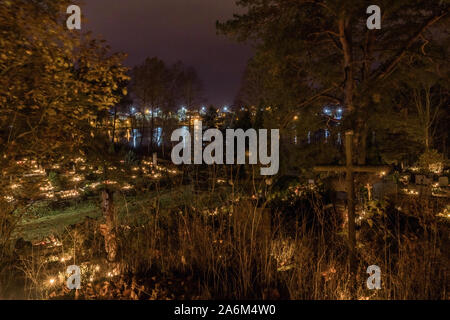 Un sacco di bruciare le candele sulle tombe tra alberi, lapidi e attraversa la sera al buio nel cimitero di Trakai, Lituania. In distanza-lago Foto Stock