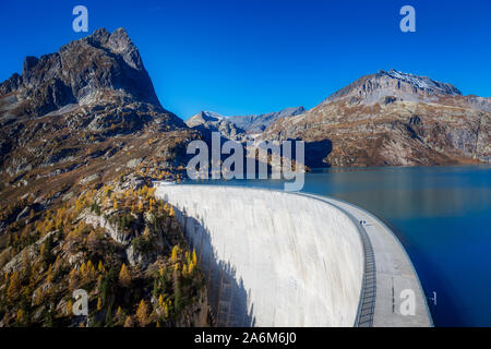 Strada di montagna su una diga e cielo blu in uno splendido paesaggio autunnale delle Alpi svizzere, Vallese, Emossson, Svizzera, Europa. Foto Stock