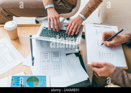 Lo sviluppatore di software digitando mentre il suo collega facendo schizzi di interfaccia Foto Stock