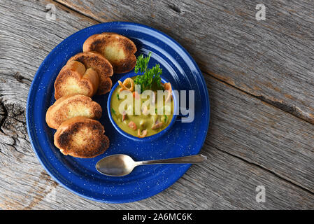 Alta angolazione di una tazza di freschi fatti in casa dividere la zuppa di piselli con pane tostato aglio su una tavola in legno rustico con copia spazio. Foto Stock