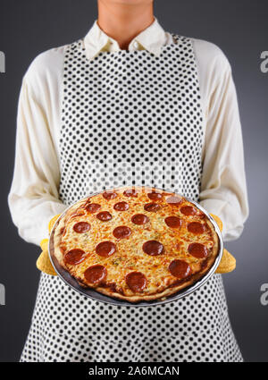 Primo piano di una massaia in un grembiule e guanti da forno tenendo freschi fatti in casa la pizza. La donna è irriconoscibile. Foto Stock