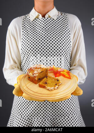 Primo piano di una massaia in un grembiule e guanti da forno in legno di contenimento piatto di portata con silced pane di zucca Foto Stock