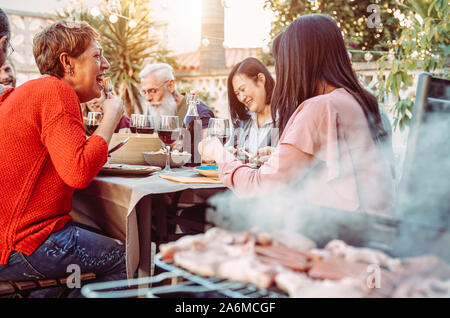 La famiglia felice di mangiare e di bere vino a cena con barbecue in giardino - Persone con differenti età cenare insieme a pranzo a barbecue Foto Stock