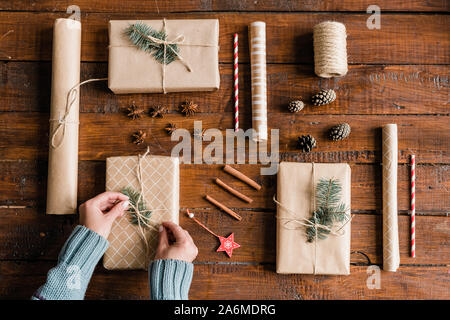 Le mani della giovane donna in blu maglione rendendo il nodo sulla sommità di uno di giftboxes Foto Stock