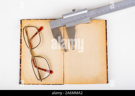 Pinza e vecchio libro con gli occhiali su un tavolo bianco. Accessori per Officina. Sfondo chiaro. Foto Stock