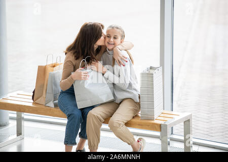 Giovane madre affettuoso bacio la sua graziosa figlia sulla guancia mentre a riposo Foto Stock
