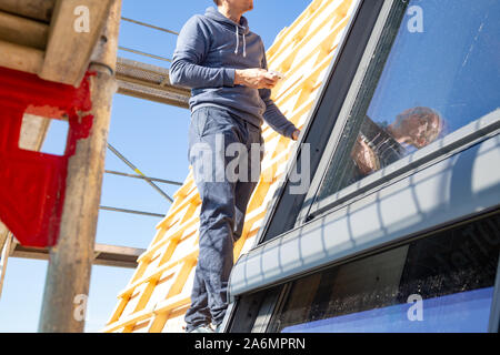 Giovane falegname installando un lucernario su un tetto di legno architrave Foto Stock