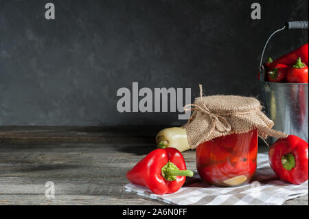 In casa i peperoncini sott'aceto e campana dolce peperone rosso sul tavolo rustico. Vaso di vetro con le conserve di pepe rosso. Background creativo per diversi scopi. Foto Stock