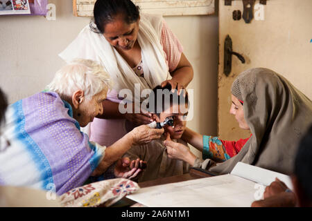 Il dottor Ruth Pfau osservando un giovane paziente che soffre di disabilità mentale. La madre del bambino è visto cercando di persuadere suo figlio per consentire Dr.Pfau per completare il check-up. Foto Stock