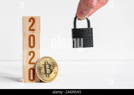 I numeri 2020 su cubi di legno, sfondo bianco accanto alla moneta bitcoin, serratura. Il concetto di domanda di tutela cryptocurrency nel nuovo anno. Close up.