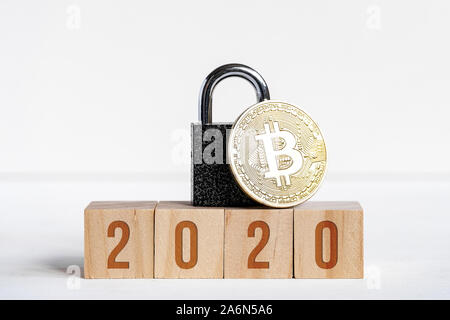 Le figure 2020 su cubi di legno su sfondo bianco accanto alla moneta bitcoin, blocco nero. Il concetto di protezione cryptocurrency nel nuovo anno. Close up.