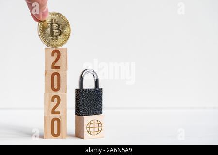 I numeri 2020 su cubi di legno, sfondo bianco accanto alla moneta bitcoin. Il concetto di domanda cryptocurrency intorno al mondo nel nuovo anno. Copia dello spazio. Foto Stock