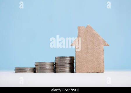 Abstract casa di cartone accanto a una pila di monete. Immobiliare di concetto di risparmio. Close up. Foto Stock
