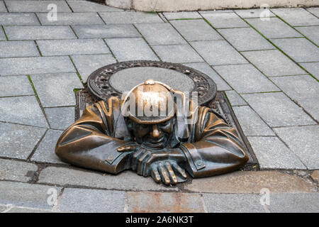 Bizzarra statua di bronzo di un lavoratore di fognature in appoggio sulla parte superiore di un tombino, "peeping' a passanti da Viktor Hulik nel quartiere del centro storico di Bratislava Foto Stock