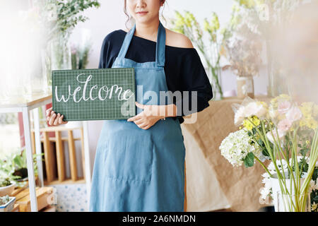 Immagine ritagliata di fiori di proprietario di un negozio di plastica di contenimento cartello con chalk iscrizione e accoglienza clienti Foto Stock