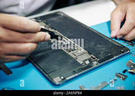 Close-up di immagine repairman utilizzando le pinzette per installazione di microchip nel computer tablet Foto Stock