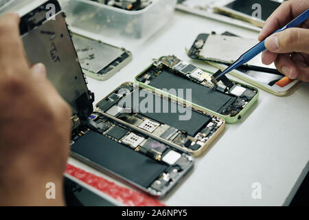 Repairman utilizzando lo smartphone fissa come riferimento durante la riparazione di due altri telefoni Foto Stock