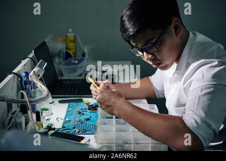 Grave repairman vietnamita in bicchieri ricerca per i dettagli dello smartphone in scatola di plastica Foto Stock