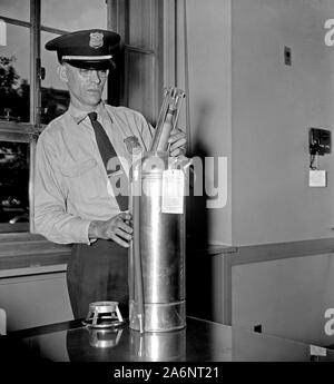 Un funzionario del Dipartimento di Giustizia protezioni, esamina un nuovo tipo di estintore cartuccia, la cartuccia è riempita con gas di biossido di carbonio ca. 1937 Foto Stock