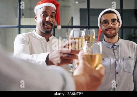 Felice i colleghi il tintinnio con gli occhiali sul vino spumante quando celebra il Natale in ufficio Foto Stock