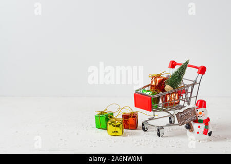 Carrello con albero di Natale in miniatura e confezioni regalo e pupazzo di neve sulla neve bianca tavolo in legno. Natale e Anno Nuovo tempo di shopping concetto. Foto Stock