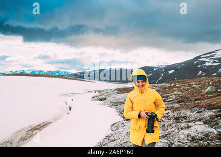 Aurlandsfjellet, Norvegia. Felice giovane donna Tourist Traveler fotografo con fotocamera Camminare vicino a Aurlandsfjellet Scenic Percorso Road. Uno stile di vita attivo Foto Stock