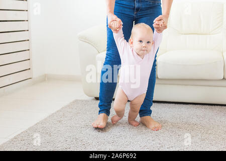 Baby prendendo i primi passi con aiuto-madre a casa Foto Stock