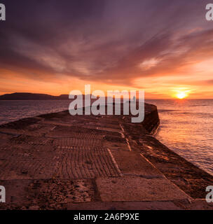 Lyme Regis, Dorset, Regno Unito. 28 ott 2019. Regno Unito Meteo: bellissima alba presso il Cobb Lyme Regis. Un uomo guarda su come il cielo sopra la storica parete Cobb si illumina con colori brillanti su una fredda mattina autunnale. Credito: Celia McMahon/Alamy Live News Foto Stock