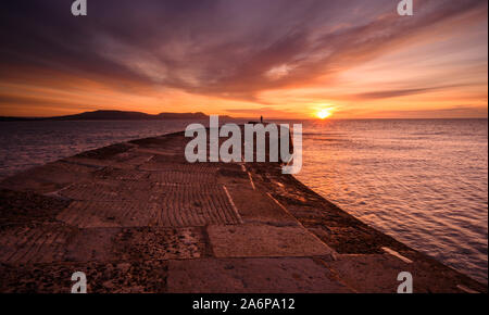 Lyme Regis, Dorset, Regno Unito. 28 ott 2019. Regno Unito Meteo: bellissima alba presso il Cobb Lyme Regis. Un uomo guarda su come il cielo sopra la storica parete Cobb si illumina con colori brillanti su una fredda mattina autunnale. Credito: Celia McMahon/Alamy Live News Foto Stock