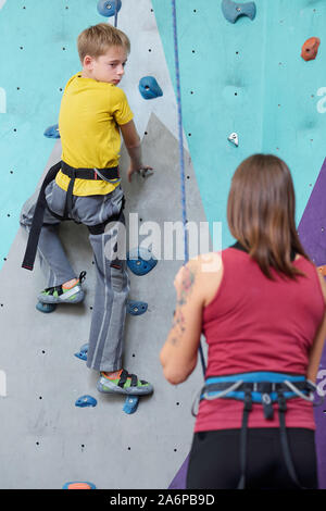 Ragazzo attivo in giallo maglietta e pantaloni grigi guardando al suo istruttore consigli Foto Stock