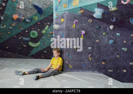 Giovane ragazzo guardando le sue mani mentre è seduto sul tappeto da arrampicata attrezzature Foto Stock