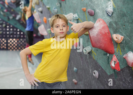 Ragazzo carino che mostra il pollice mentre appoggiata da arrampicata attrezzature Foto Stock