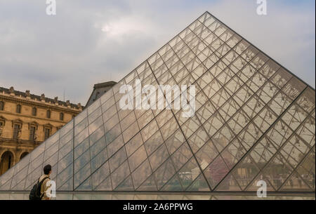 Un visitatore maschio con lo zaino si erge davanti alla piramide del Louvre, guarda fino alla punta e ammira la contemporanea costruzione in vetro a Parigi. Foto Stock