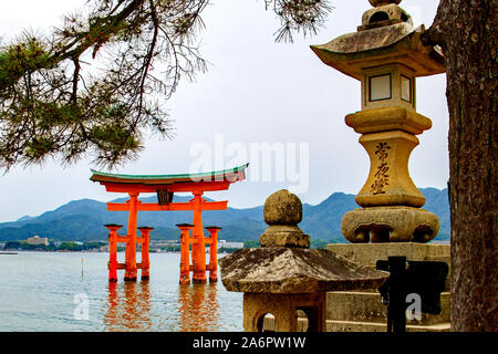 Giapponese lanterne di pietra con la floating torii gate del santuario di Itsukushima nel mare di Miyajima island, Giappone Foto Stock