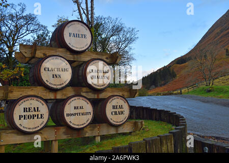 Editoriale di Clachaig Inn, Glencoe, Highlands scozzesi, pubblicità sui barili di birra a fronte dell'Inn. Montagna e strada in background. Foto Stock