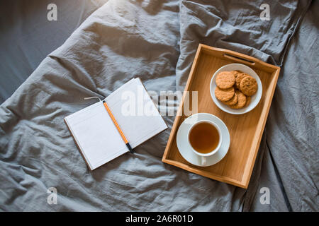 La prima colazione di tè e biscotti con un blocco note e penna in un letto di grigio al mattino Foto Stock