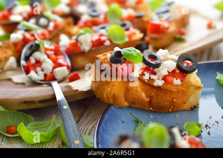 Calda bruschetta greca: croccante cotta piccole fette di pane pita con il formaggio feta, olive nere, peperoncino e basilico, servita come antipasto Foto Stock