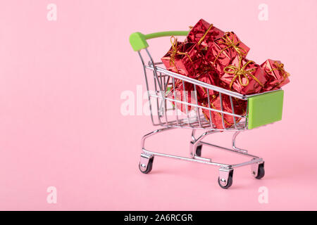 Mini green shop carrello con piccole confezioni regalo su sfondo rosa, la copia in bianco di spazio, vicino. Shopping di Natale concept Foto Stock