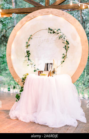 Nozze arco tondo in stile rustico decorato con ghirlande di fiori e vegetazione, retro lampadine sul soffitto. Bellissimo matrimonio istituito. Area Foto Stock