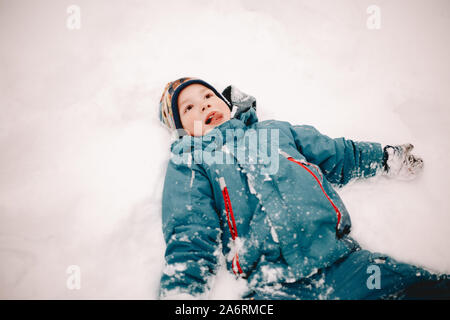 Felice Ragazzo spuntavano lingua mentre giaceva nella neve in inverno Foto Stock