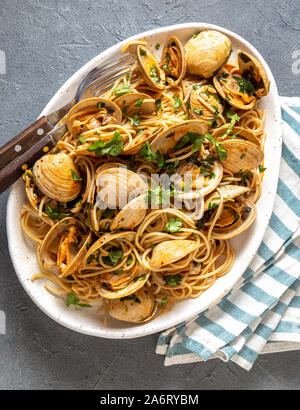 Piatti di pasta. ITALIAN spaghetti alle vongole. Spaghetti vongole sulla piastra bianca con vino bianco e sfondo grigio. Vista superiore Foto Stock